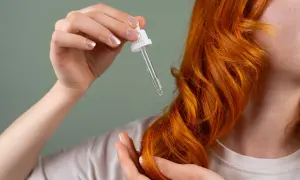 Dłoń z pipetką z olejkiem aplikuje pielęgnację na rude włosy. Dowiedz się, jak często olejować włosy dla najlepszych efektów.
