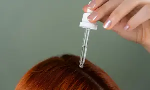 Dłoń z pipetką aplikuje serum na skórę głowy, wspierając etapy odrastania włosów po chemioterapii.