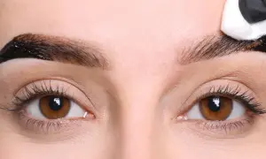 Aplikacja henny pudrowej na brwi. Widoczne brązowe oczy i proces stylizacji brwi, który daje naturalne henna pudrowa efekty.
