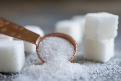 Łyżeczka z kryształkami, obok kostki cukru. Czy to sorbitol? Ten słodzik jest często używany jako zamiennik cukru.