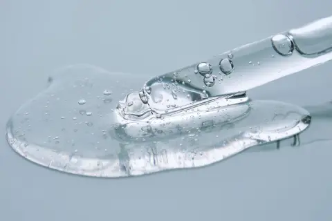 Kropla przejrzystego serum z pęcherzykami powietrza, zawierającego peptydy i ceramidy, spływa z pipety.