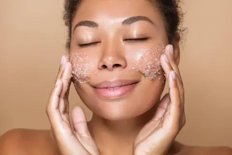 Kobieta z zamkniętymi oczami delikatnie masuje twarz peelingiem. To właśnie jest peeling – sposób na gładką skórę.