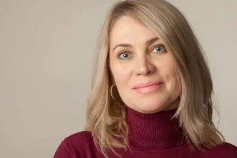 Kobieta po 50-tce z niebieskimi oczami i blond włosami, zastanawiająca się nad zabiegami na twarz.