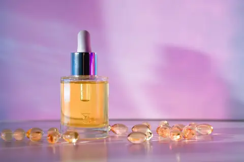Serum z retinalem i kapsułki z retinolem na różowym tle.