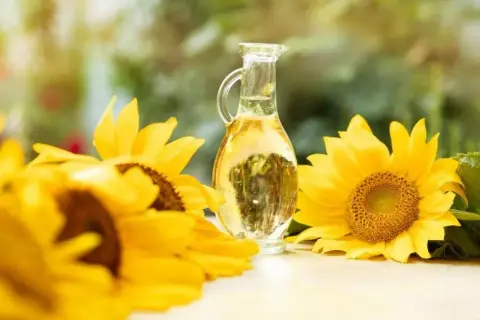 Słonecznikowy olej (helianthus annuus seed oil) w karafce, otoczony przez piękne, żółte słoneczniki.