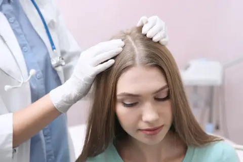 Lekarz od włosów bada skórę głowy pacjentki.