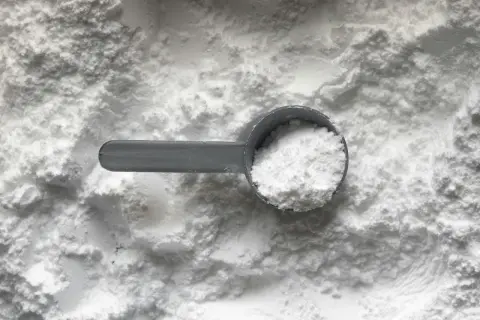 Miarka z białym proszkiem, prawdopodobnie tetrasodium glutamate diacetate, na tle sypkiego materiału.