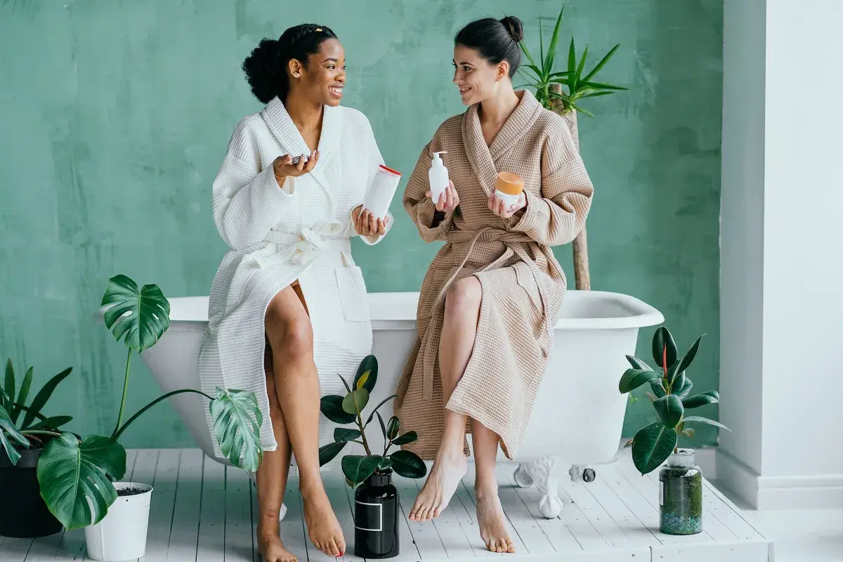 Dwie kobiety w szlafrokach siedzą przy wannie, trzymając kosmetyki. Czy to amoniak? Nie, to pielęgnacja.